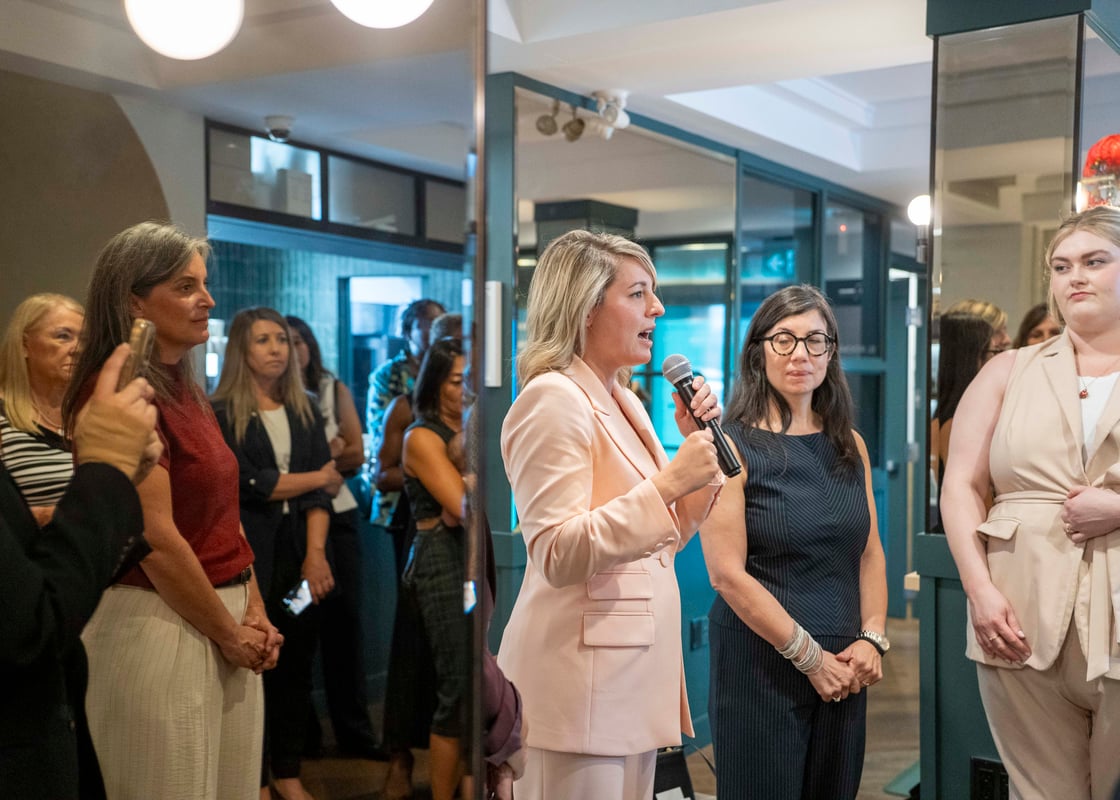 The Honourable Mélanie Joly, speaks into a microphone and addresses a room of attendees at a reception for the roundtable on Women, Capital, and Canada's Economic Future.